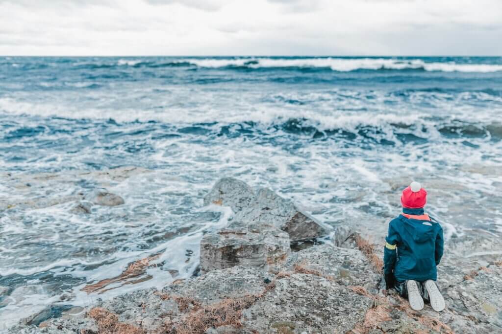 person kneeling humbly while overlooking the vastness of the ocean.