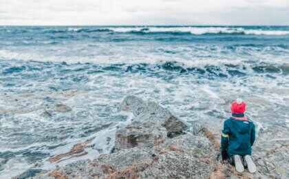person kneeling humbly while overlooking the vastness of the ocean.