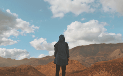 A woman standing at the edge of a cliff or mountain, looking out towards a vast horizon. Representing overcoming challenges and seeing the broader perspective of life.