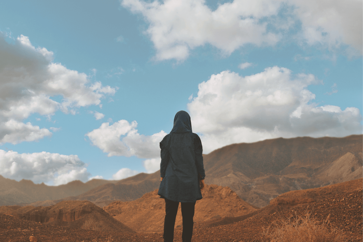 A person standing at the edge of a cliff or mountain, looking out towards a vast horizon. A woman standing at the edge of a cliff or mountain, looking out towards a vast horizon. Representing overcoming challenges and seeing the broader perspective of life.