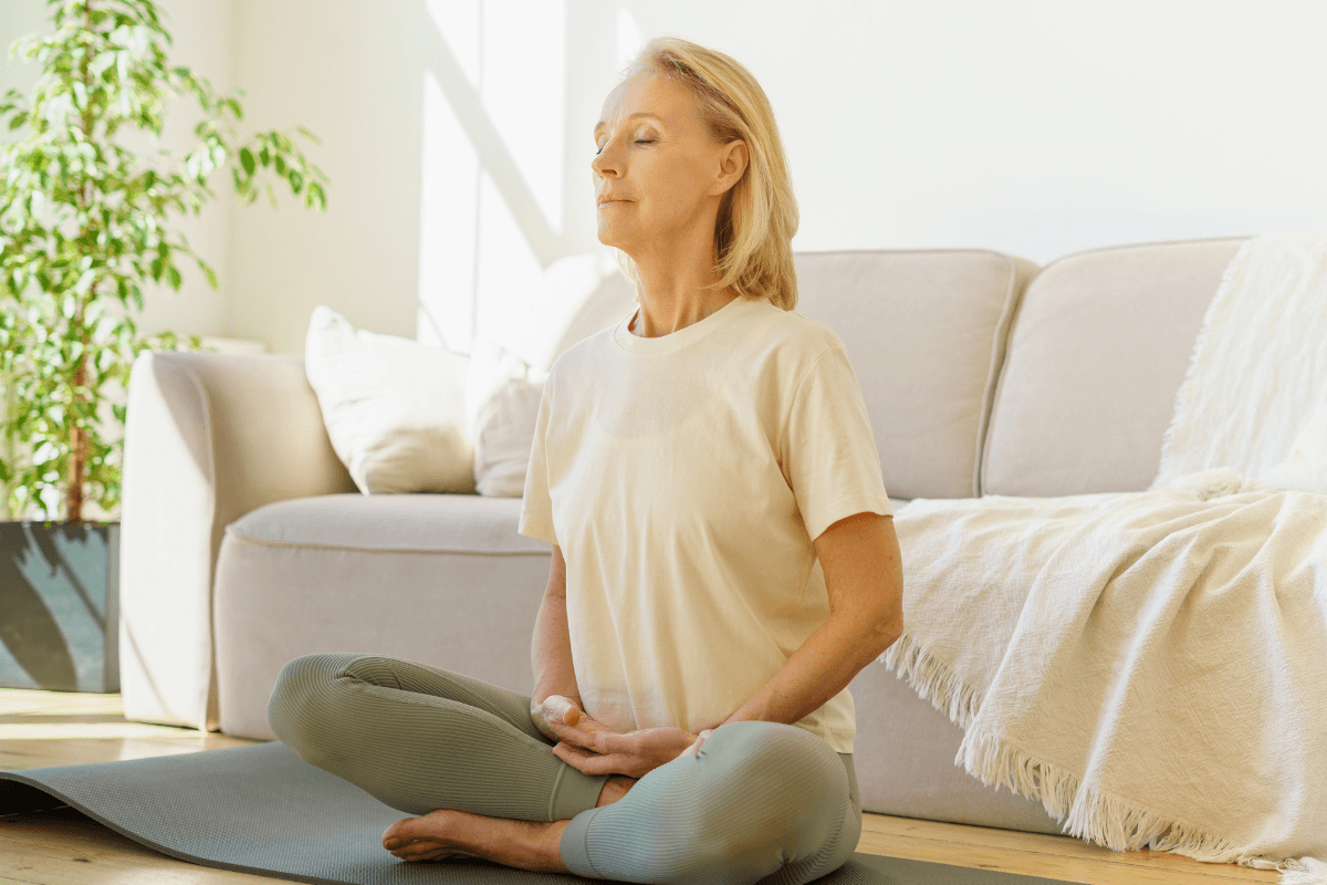 Midlife Woman practicing mindfulness Midlife Woman sitting cross-legged on a mat practicing mindfulness