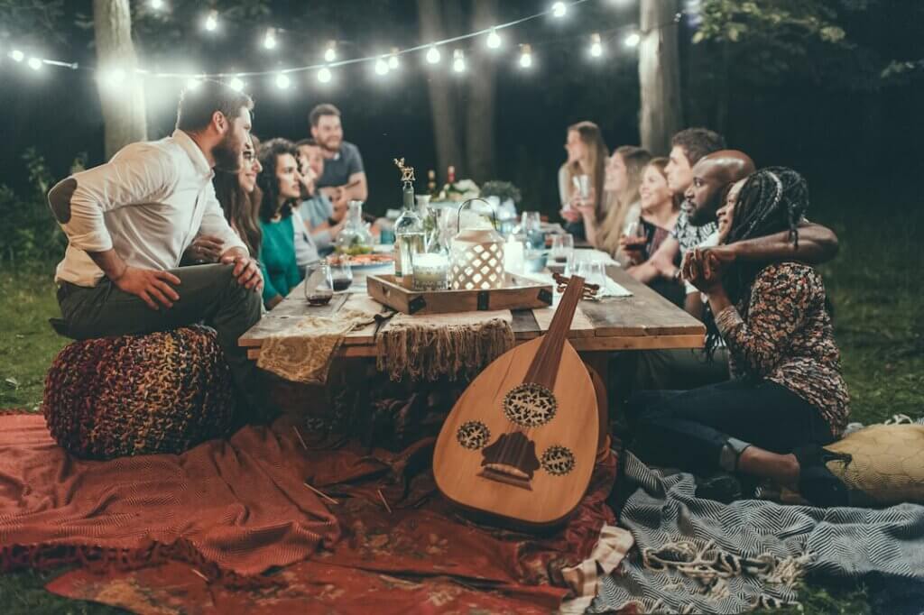 People gathered around an outdoor table at night under string lights, sharing food and conversation &mdash; symbolizing community, stability, and connection.