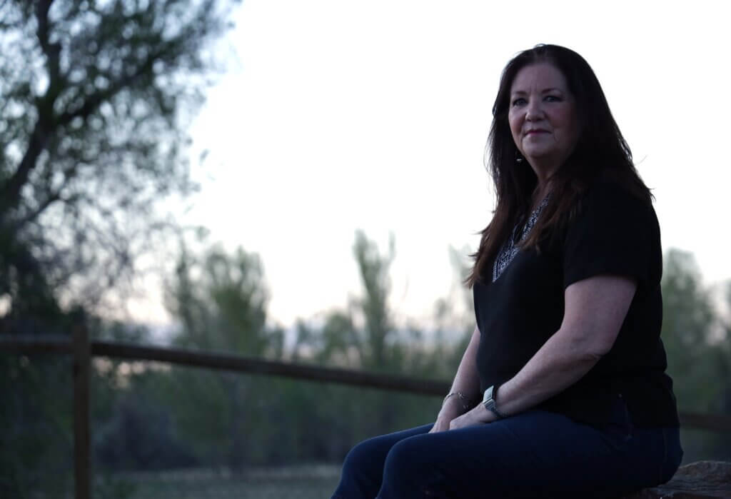 Kelli Nelson seated outdoors at dusk, looking ahead with a composed expression