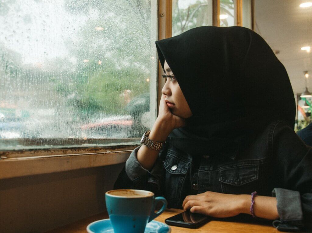 Woman sitting at caf&eacute; table looking out rainy window in quiet reflection