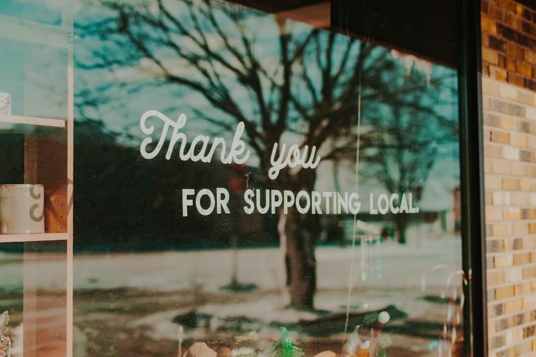 Storefront window with a hand-lettered sign thanking customers for supporting local business